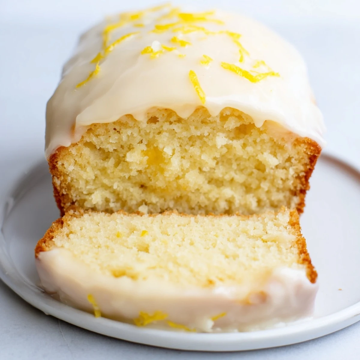 A close-up of a golden Lemon Loaf Cake, drizzled with bright, glistening lemon icing.