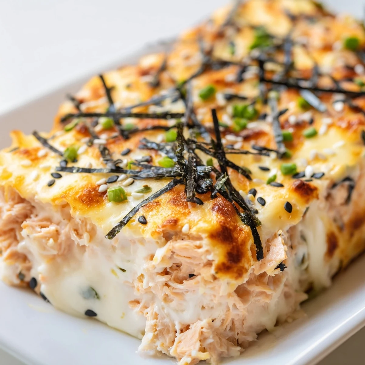 Creamy Salmon Sushi Bake topped with melted cheese, sesame seeds, and fresh green scallions, ready to eat.