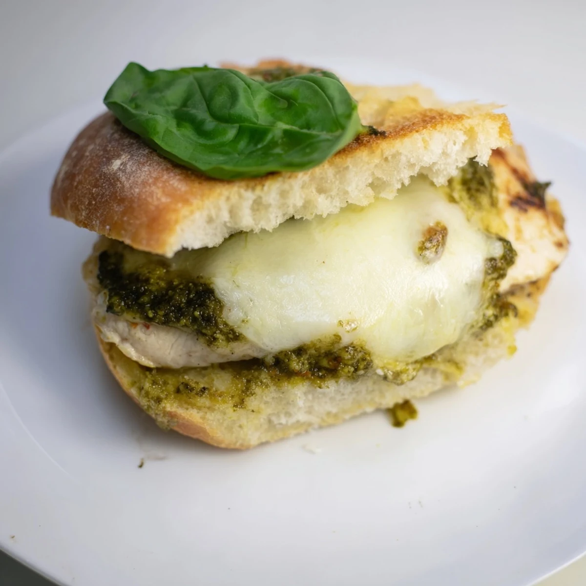 Fresh basil leaves and sliced tomatoes garnish the Pesto Chicken Melt, served hot with a side of chips.