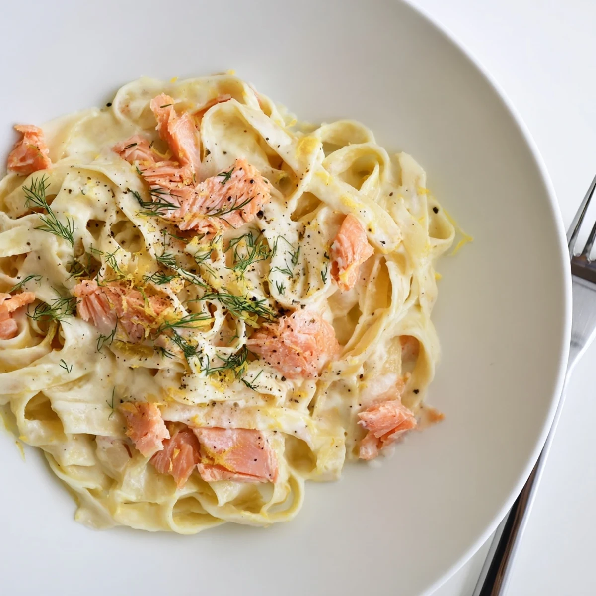Golden creamy salmon pasta garnished with fresh dill and lemon zest, served hot alongside a crisp green salad.