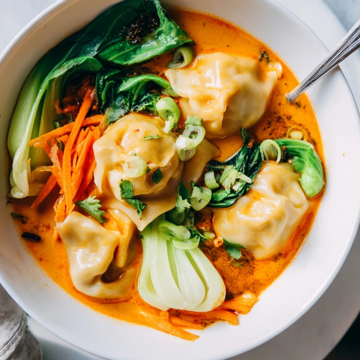 A bowl of steaming Red Curry Wonton Soup with Greens, fragrant coconut broth ladled over tender wontons and fresh spinach.  