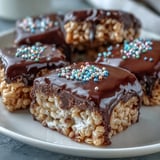 Freshly cut squares of Chocolate Covered Rice Krispy Treats arranged on a white plate, perfect for parties or family dessert sharing.