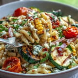 Colorful summer pasta salad featuring smoky grilled zucchini, fresh corn, and tangy Cotija cheese tossed with cherry tomatoes.  