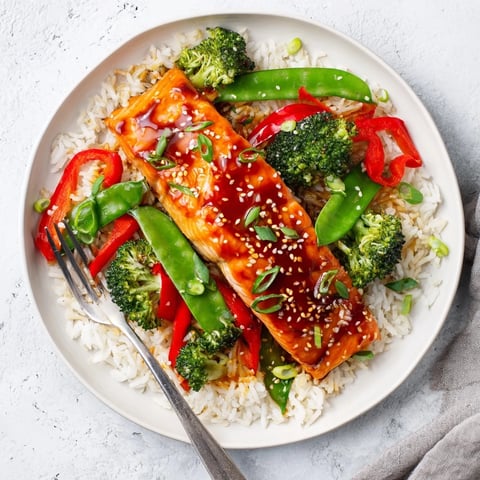 Flaky Maple Soy Glazed Salmon rests on a bed of fluffy rice with crisp-tender broccoli, snap peas, and red bell peppers.  