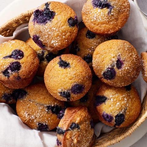 Fluffy mini blueberry muffins, golden-brown and ready to eat, are presented in a rustic basket.