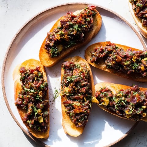 Close-up of vibrant black olive tapenade, speckled with herbs, served with toasted crostini for dipping.