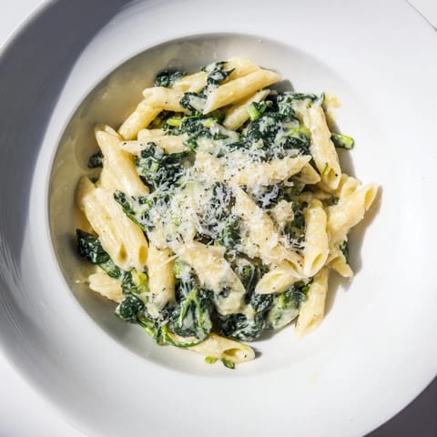 A steaming bowl of creamy spinach pasta, sprinkled with Parmesan, offering a delightful aroma.
