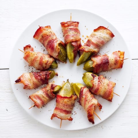 Twelve crispy, smoky bacon-wrapped pickle halves arranged neatly on a baking sheet fresh from the oven.