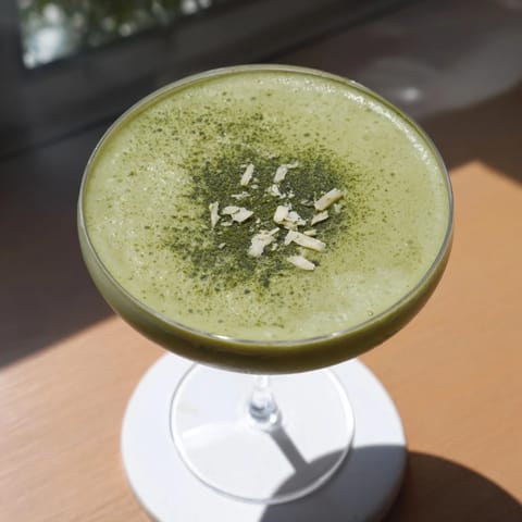 Creamy Matcha Martini with a smooth, earthy flavor, garnished with delicate white chocolate shavings for a sweet finish.  