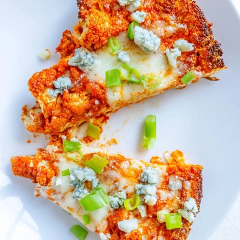 A close-up of Buffalo Cauliflower Pizza slices with tangy buffalo sauce, bubbling cheese, and celery garnish, perfect for a vegetarian dinner.