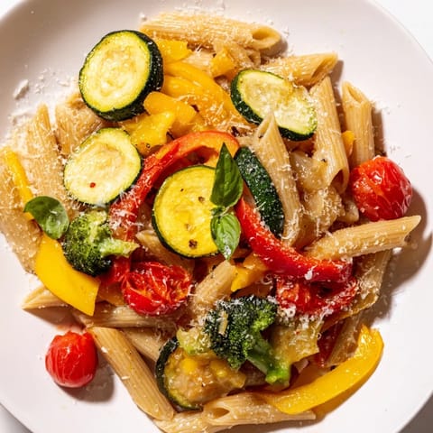 A close-up of vibrant vegetarian pasta primavera, featuring al dente fusilli, colorful roasted vegetables, and a generous sprinkle of Parmesan cheese.