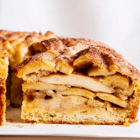 A rustic casserole-style Dutch Baked Apple Cake, golden-brown and spiced, cooling slightly on a wooden board before serving.