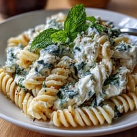 Creamy Pea and Ricotta Pasta with Mint, garnished with Parmesan and fresh herbs, served in a white bowl.  