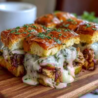 Miniature Derby Party Hot Brown Sliders on buttery brioche buns, layered with turkey, bacon, and creamy Mornay sauce, baked golden for a Southern appetizer.