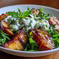 Juicy grilled peaches paired with creamy burrata, drizzled with honey, served on a bed of fresh arugula.